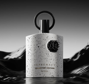 A bottle of Afnán Supremacy Collector's Edition fragrance, featuring a textured white bottle with black speckles, a black circular cap handle, and gold lettering, set against a dark, moody mountain background.