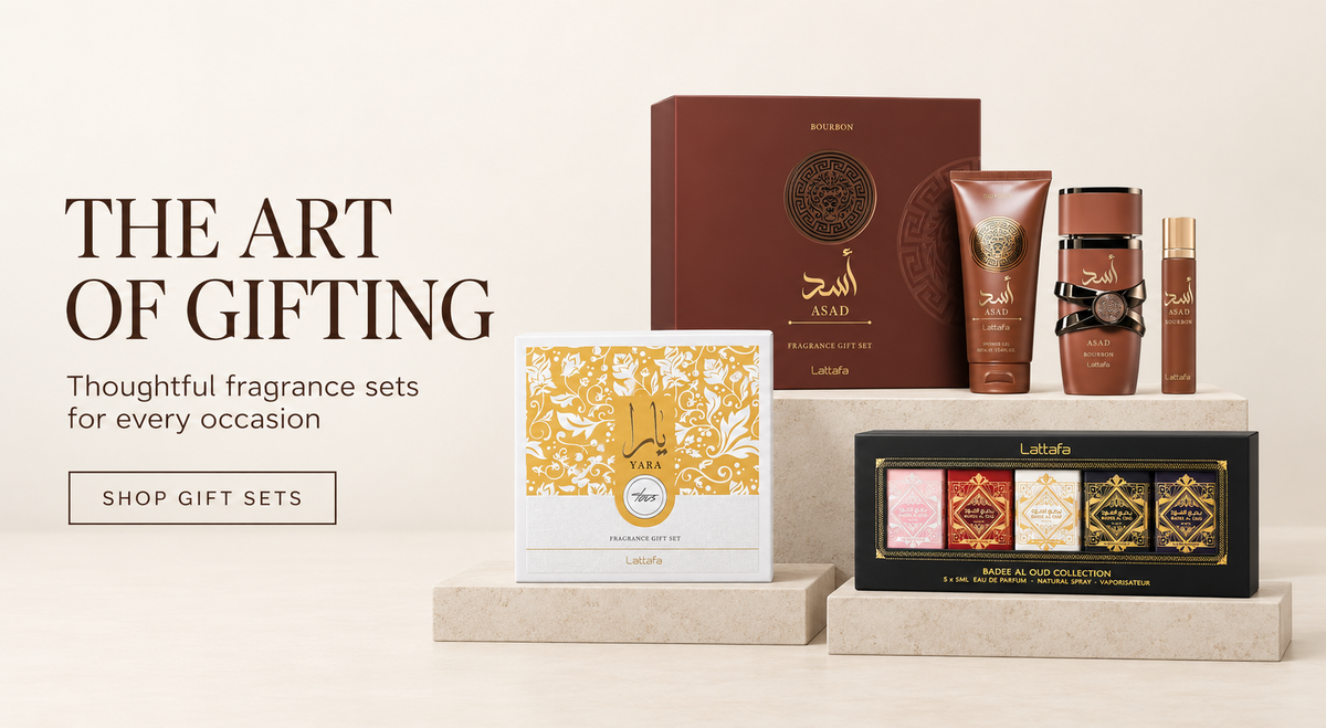 A curated fragrance gift set displayed on pedestals against a warm beige background, with promotional text reading 'THE ART OF GIFTING.' The set includes a large brown box, a white box with ornate gold patterning, several brown cylindrical bottles, a small gold bottle, and a black rectangular set containing four colorful decorative boxes.